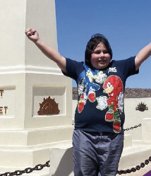 A participant on an outing, arms raised beside a monument